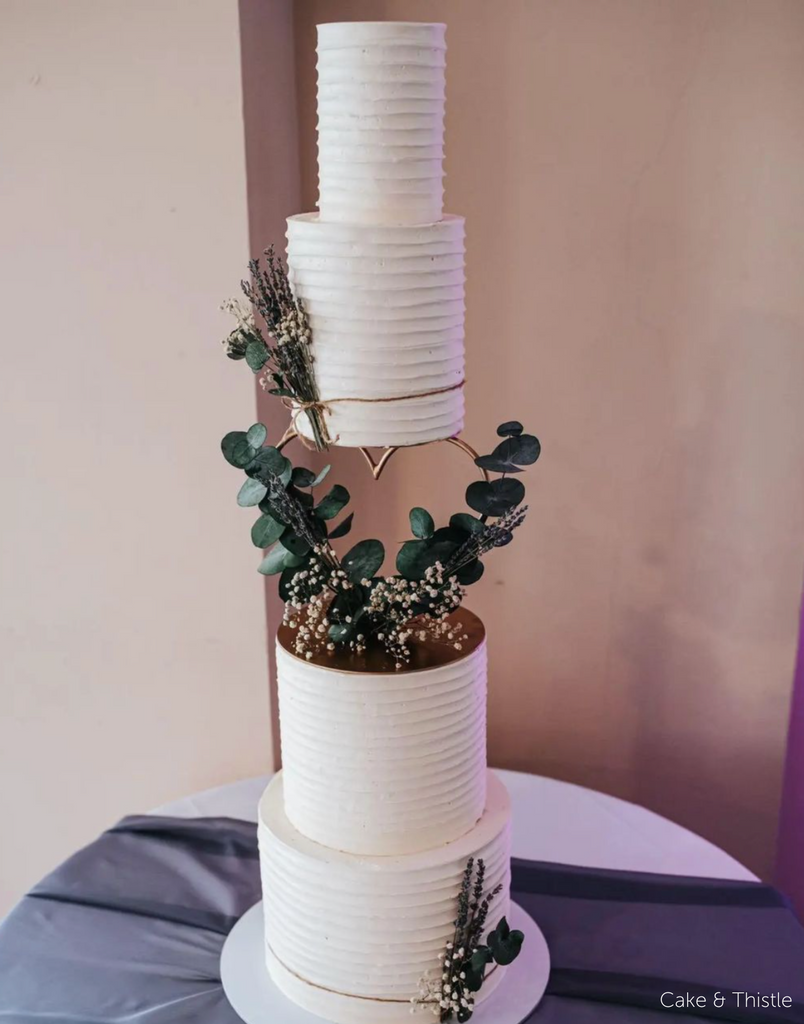A stripey white four tier cake with leaves placed on it, the middle two layers are separated by a Heart Tier Separator - Prop Options