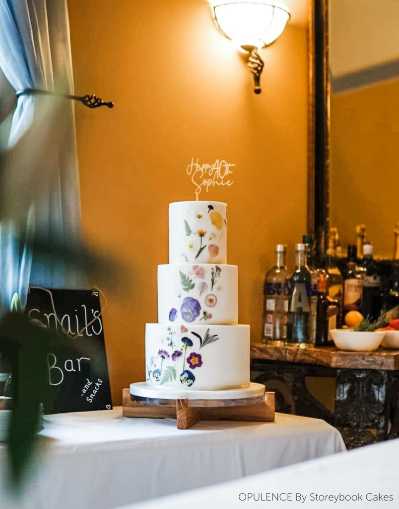 A white three layer cake with floral decorations stood on a Handcrafted Solid Oak Cake Stand - Prop Options