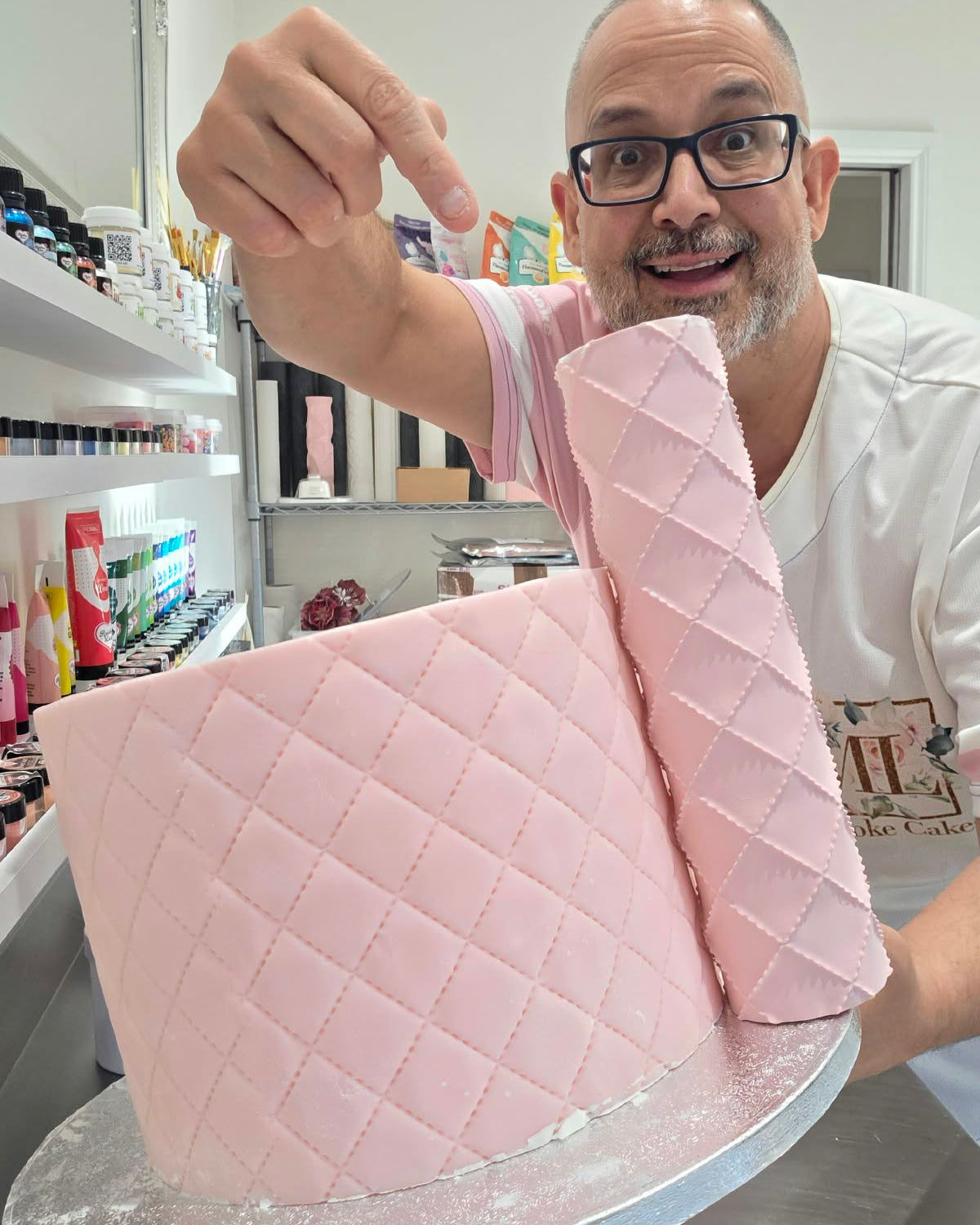 Victor Diaz pointing at the Quilted diamond pattern rolled around a pink fondant cake with a rolled fondant sheet beside it - Prop Options