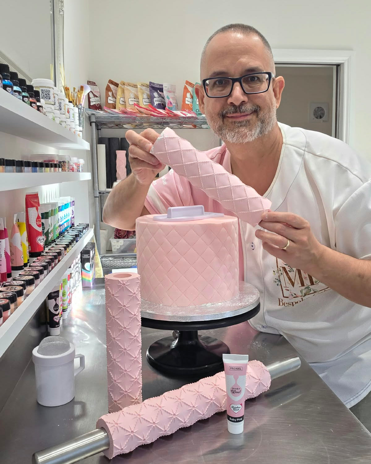 Victor Diaz holding the Quilted rolling pin pattern rolled in pink fondant beside a quilted cake, with the Quilted Pearl pins on the bench - Prop Options