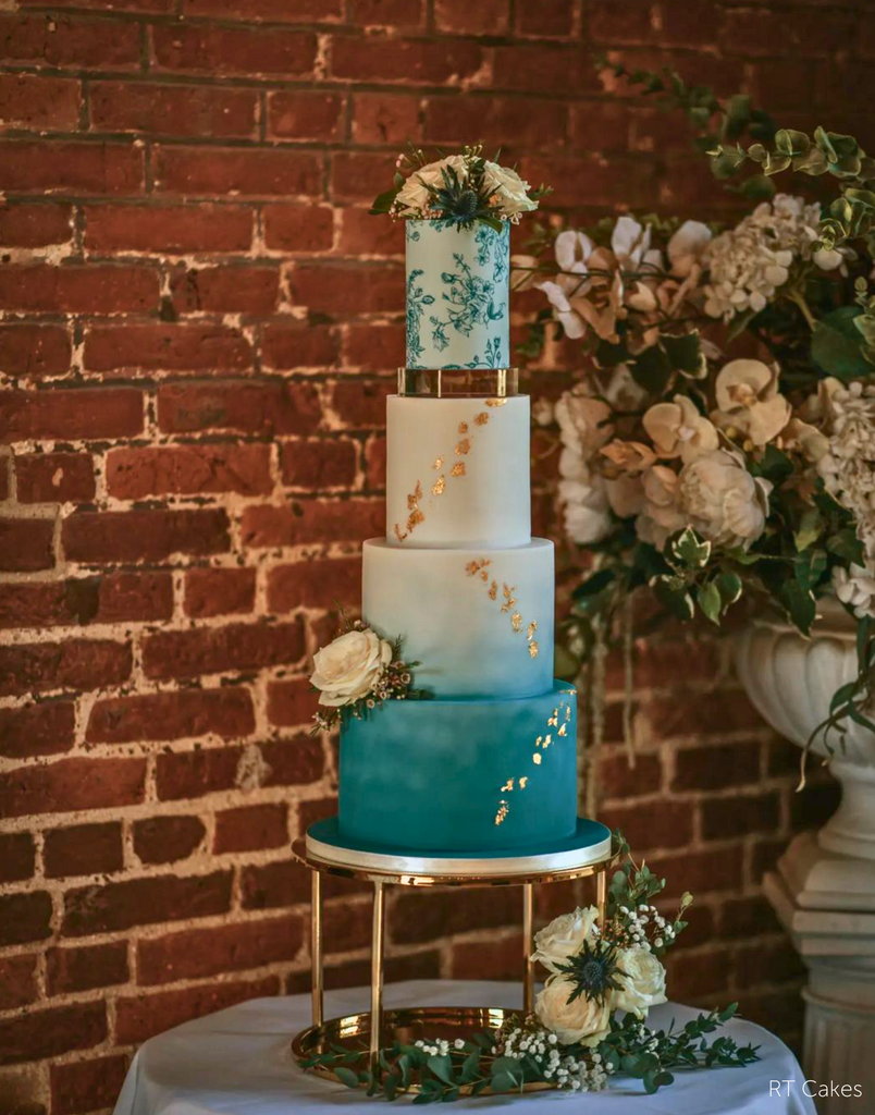 Gold Round Metallic Plinth holding up a multitiered cake in various shades of blue with gold decorations and white flowers - Prop Options