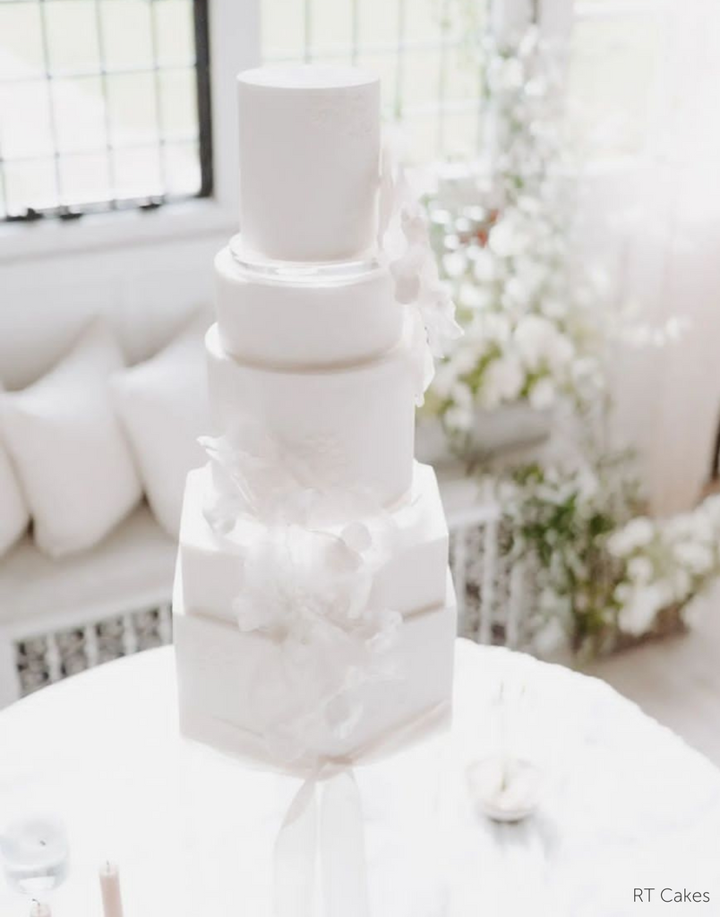 A completely plain white multitiered cake with round upper layers and hexagonal bottom layers, the layers are separated with a 15mm Acrylic Cake Separator - Prop Options