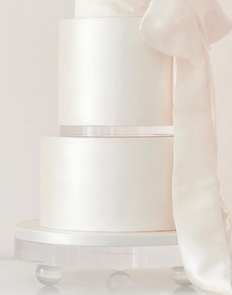 Close up of a plain white multilayer cake with a white ribbon, two of the layers are separated with a 15mm Acrylic Cake Separator - Prop Options