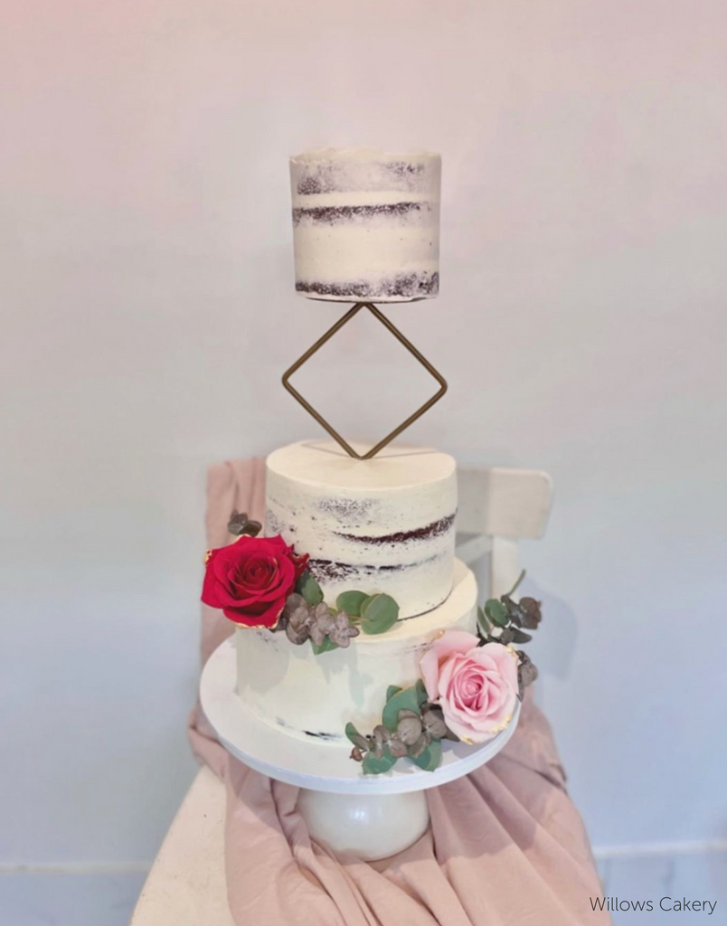 A three layer rustic white cake with red and pink roses at the base, the top two layers are separated by a Diamond Cake Spacer - Prop Options