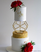 A three layer cake with white top and bottom layers and a gold middle layer, there are red roses on the top and bottom as well as gold lettering, the top two tiers are separated using a Geometric Pentagon Spacer - Prop Options