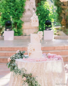 A cream coloured four tier cake with light coloured flowers on each layer, the top two layers are sepaarted by a Heart Tier Separator - Prop Options