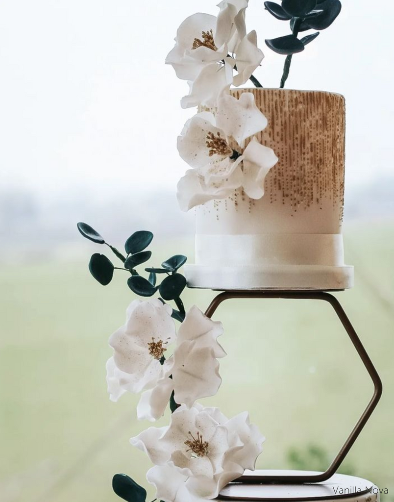 A close up of two white and brown cake tiers with white flowers being separated by a Hexagon Tier Separator - Prop Options
