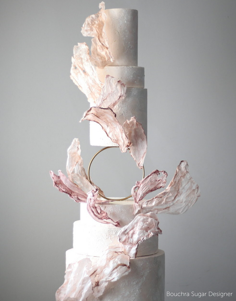 A marbled white and pink multitiered cake with delicate pink and white decorations, the middle of the cake is separated by a Hoop Tier Separator - Prop Options