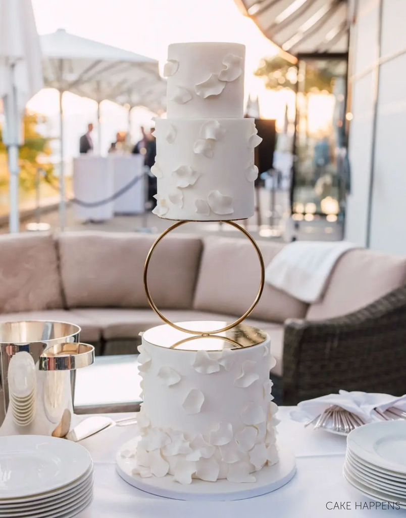 A white three layer cake with subtle petal designs on each layer, the top two tiers are separated by a Hoop Tier Separator - Prop Options
