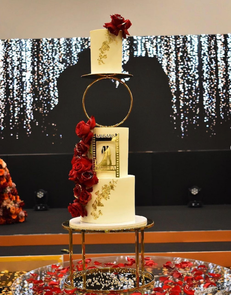 A cream coloured three tier cake with red roses, gold floral decorations, and a gold silhouette of a couple on the front, the top two tiers are separated by a Hoop Tier Separator - Prop Options