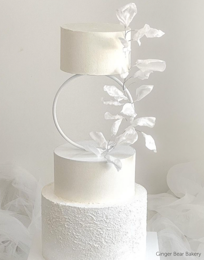 A plain white three layer cake with white flowers going up a white Hoop Tier Separator and top tier - Prop Options