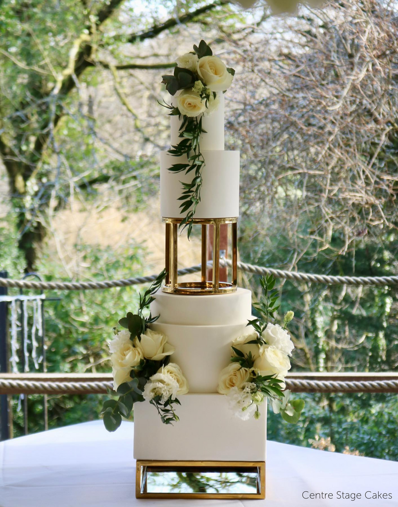 A plain white multilayered cake with white roses separated in the middle using a 6" Round Metallic Cake Spacer - Prop Options