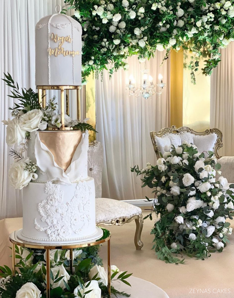 A white three tiered cake with white roses and gold lettering on the top separated by a 6" Round Metallic Cake Spacer - Prop Options