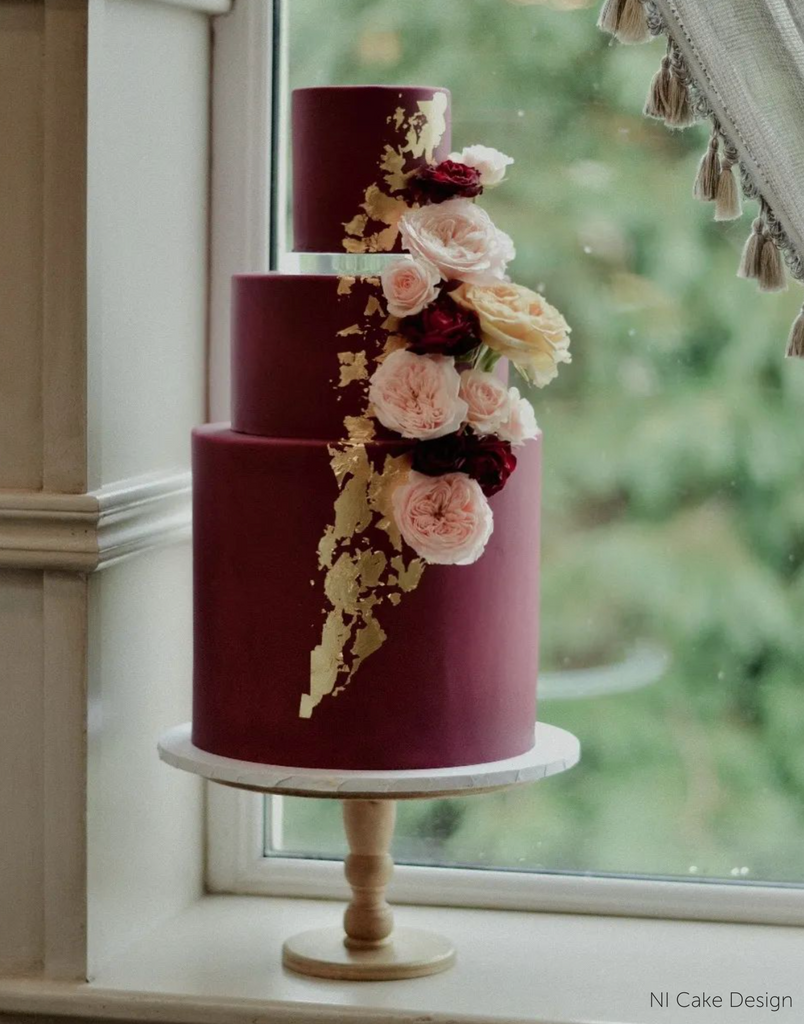 A burgundy cake with gold accents and light coloured flowers stood on The Original Scandinavian Birch Cake Stand - Prop Options