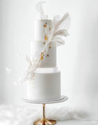 A plain white cake with subtle gold decorations and white fabric, the bottom and middle layer are sepaarted by a 30mm Round Acrylic Cake Separator - Prop Options