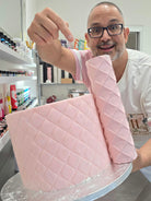 Victor Diaz pointing at the Quilted diamond pattern rolled around a pink fondant cake with a rolled fondant sheet beside it - Prop Options