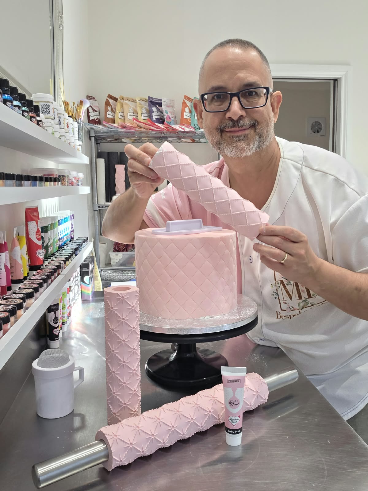 Victor Diaz holding the Quilted rolling pin pattern rolled in pink fondant beside a quilted cake, with the Quilted Pearl pins on the bench - Prop Options