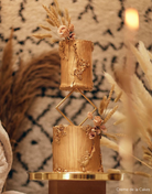 A gold coloured two tier cake with gold decroations and florals, the tiers are separated using a gold Diamond Cake Spacer - Prop Options