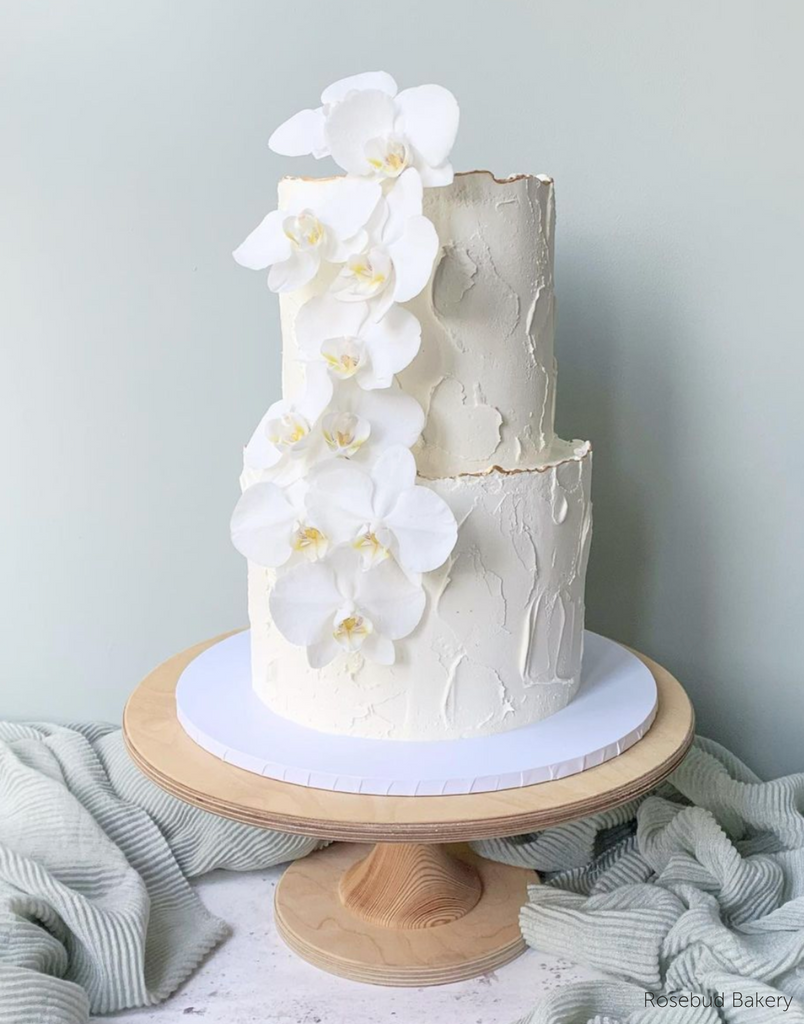 A white cake with white flowers stood on The Hourglass Scandinavian Birch Cake Stand - Prop Options