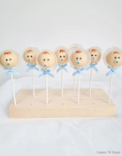 Cake pops decorated to look like baby boys with white bonnets and blue ribbons being held in an English Pine Wooden Cake Pop Stand - Prop Options