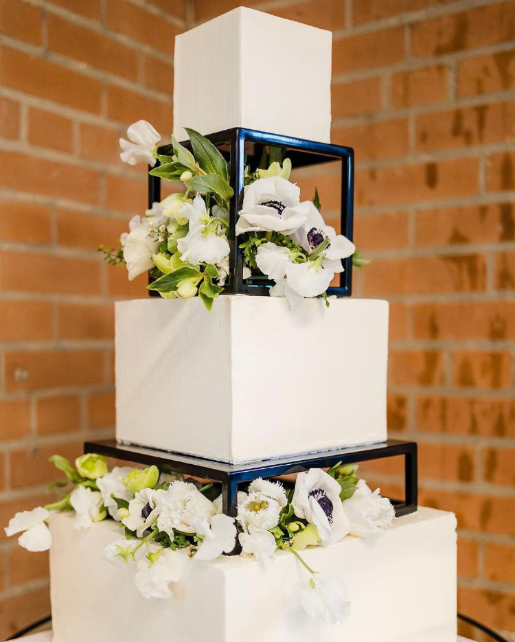 A multilayered white square cake with white flowers, each layer is separated using a Rectangle Metallic Cake Spacer - Prop Options