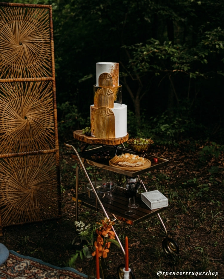 Design by Spencers Sugar Shop - exquisite detailing on gold and white cake in a forest picnic scene using Prop Options' clear tier and log slice stand