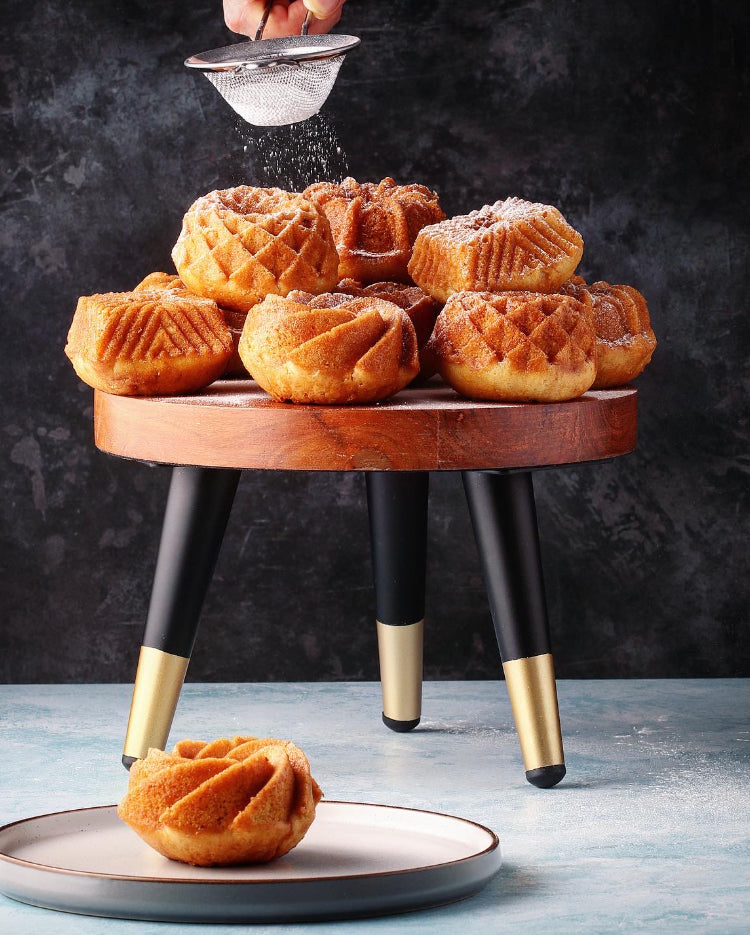 Prop Options Solid wood stand with matte black and gold tapered legs displaying stunning bakes being dressed with icing sugar