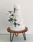 Prop Options Acacia wood hairpin leg stand supporting white tiered wedding cake